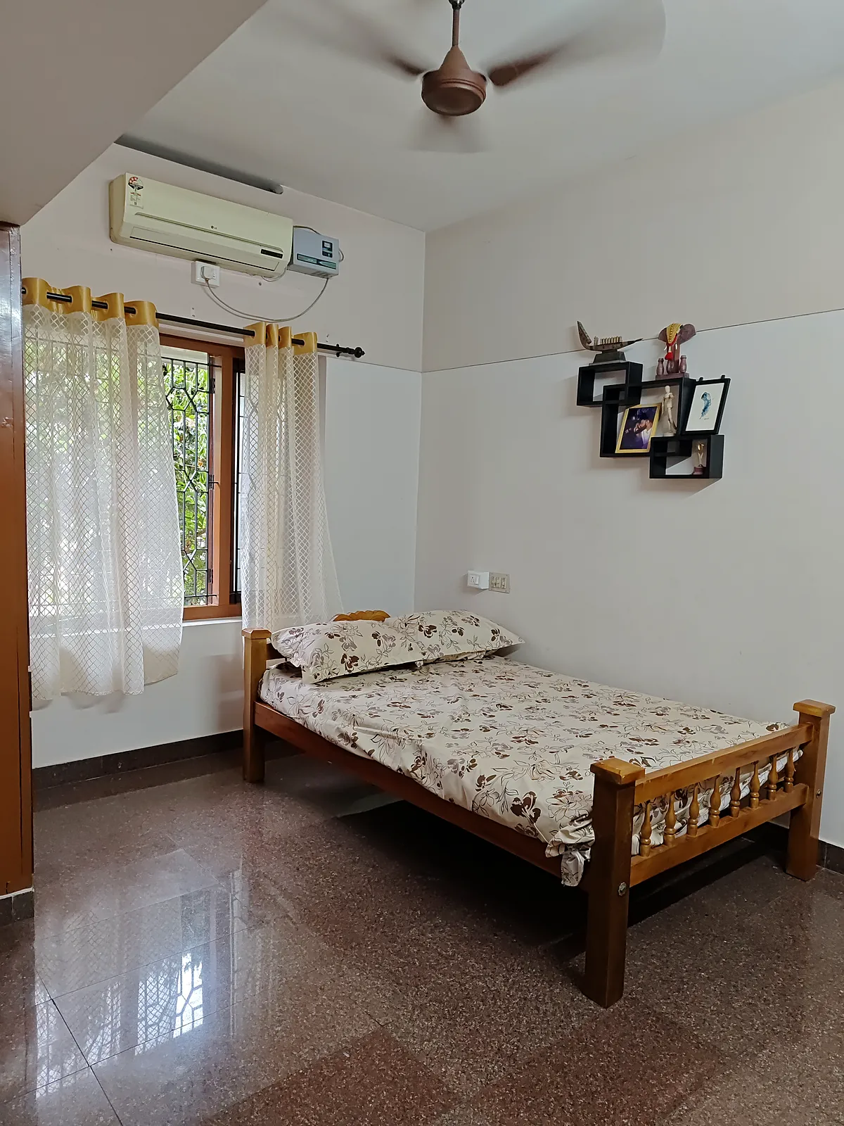 Corner bedroom on the first floor with a carved wooden bed, shelves on the wall and a window onto the trees